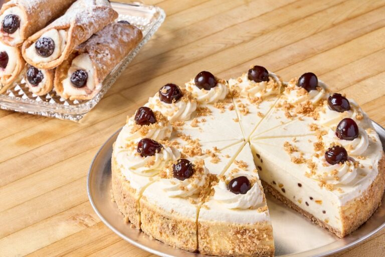 Tray of cannolis next to Cannoli Cheesecake on wooden counter