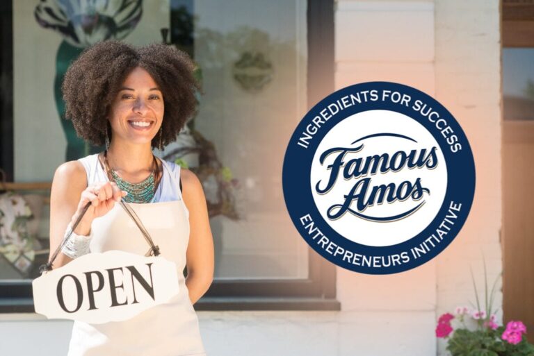 Woman standing outside business holding an 'Open' sign with Famous Amos logo in corner.