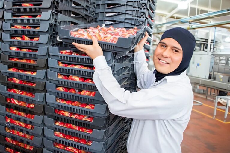 Bakery worker stacking packages of buns on a cart.