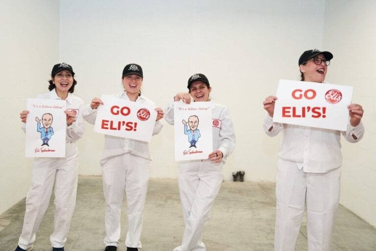 Four Eli's Cheesecake employees holding signs at bakery