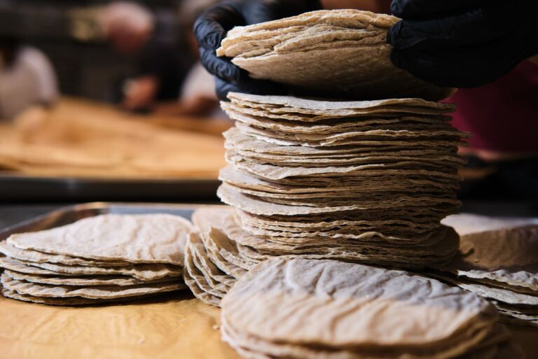 Person wearing black gloves stacking Pacha tortillas on wooden surface