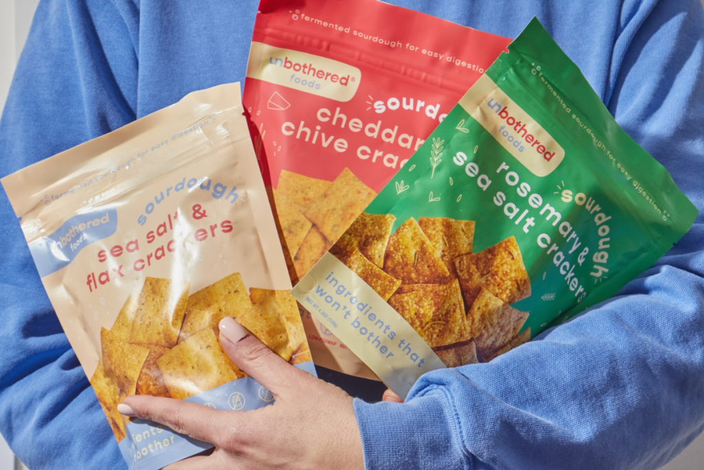 Person in blue top holding bags of Unbothered Foods sourdough crackers